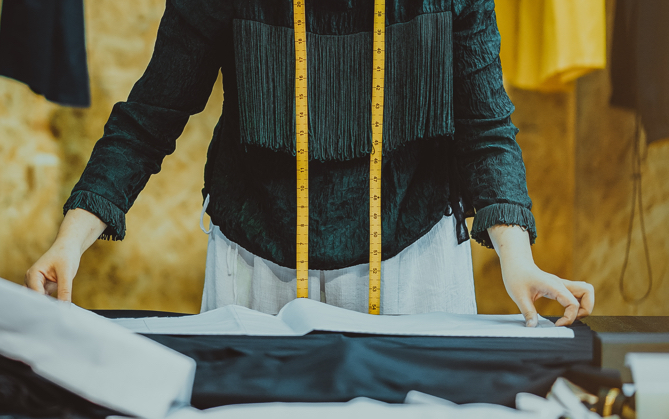 A person measuring a piece of fabric with a yellow measuring tape over their shoulders